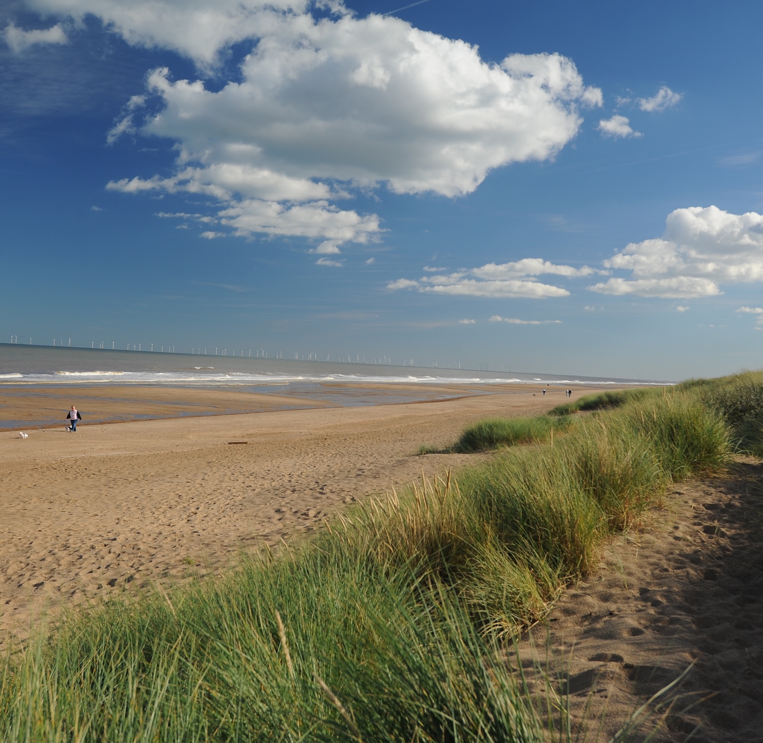 Grassy sand dunes leading down to a quiet beach with waves along the Lincolnshire coastline