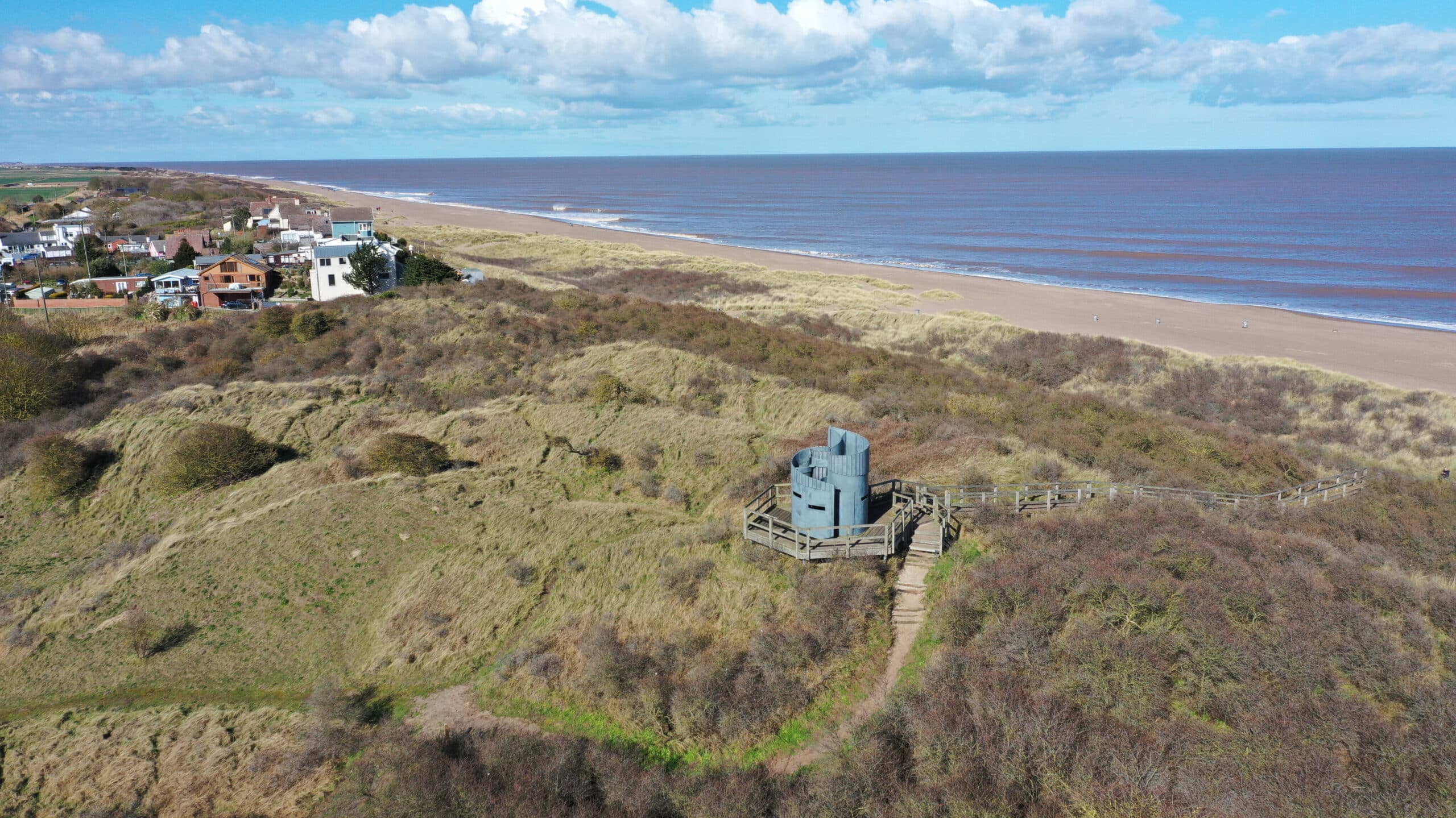 Aerial view of coastal sand dunes with seaside homes and a lookout structure along the Lincolnshire coast
